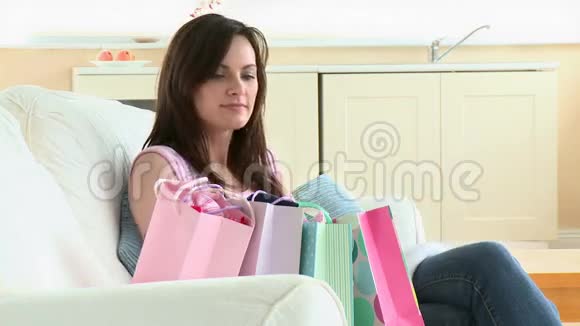 一位年轻的白种人快乐坐在沙发上打开购物袋视频的预览图