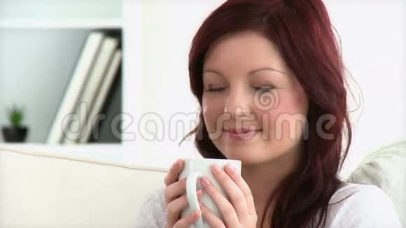 放松的女人坐在沙发上享受咖啡视频的预览图