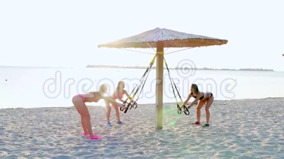 三名运动员穿泳衣的年轻女性教练用健身TRX系统做运动TRX悬架视频的预览图