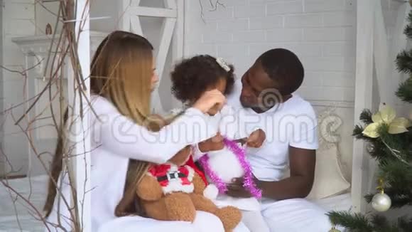 年轻幸福的多民族家庭母亲父亲和小女儿在圣诞节和圣诞节的背景下穿着白色衣服视频的预览图