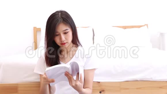 美丽的肖像年轻的亚洲女人放松坐在卧室看书在家里视频的预览图