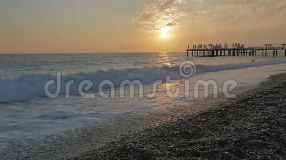 五彩缤纷的日落海浪和泡沫的海景码头和卵石海滩视频的预览图