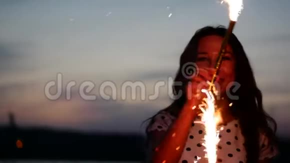 年轻快乐的微笑的女人在日落时缓慢地用火花跳舞在海滩上日落时用烟花视频的预览图