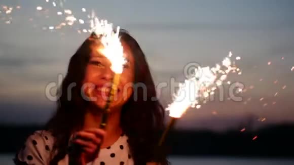 年轻快乐的微笑的女人在日落时缓慢地用火花跳舞在海滩上日落时用烟花视频的预览图