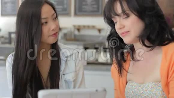 两位女性朋友在咖啡店看数字平板视频的预览图