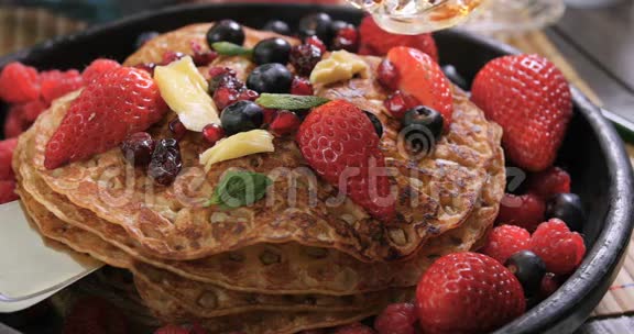 在一顿有浆果和干水果的薄煎饼的早餐加入枫糖浆视频的预览图