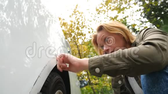 看着一辆损坏的车女金发女在车祸后检查汽车损坏4k慢镜头视频的预览图