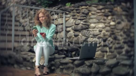 有笔记本电脑和文件的女人在石墙的背景上一杯酒和一杯酒视频的预览图
