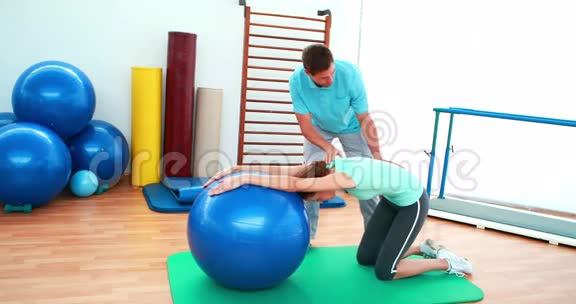 教练帮他的客户用健身球伸展背部视频的预览图