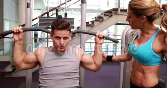 健身男子使用举重机作为他的手臂而教练监督视频的预览图