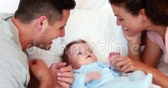穿着蓝色婴儿裤的小男孩在床上被父母挠痒痒视频的预览图