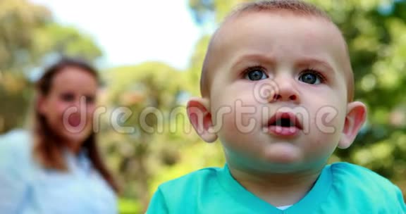 可爱的小男孩坐在草地上妈妈在他身后视频的预览图