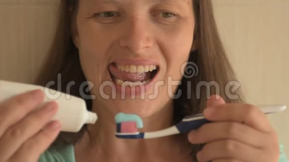 年轻女孩长着漂亮的白牙把牙膏从管子里挤出来清洁牙齿看智能手机上的信息视频的预览图