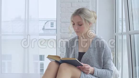 一个年轻的女孩坐在窗台上看书视频的预览图