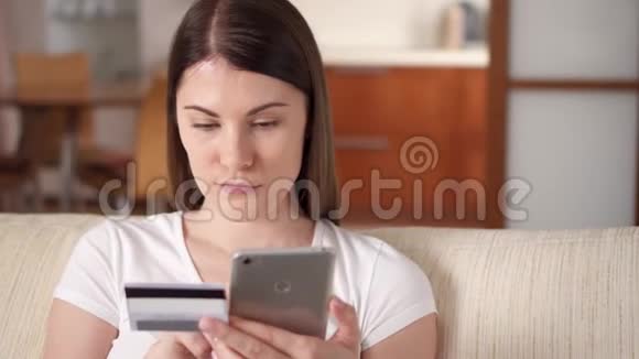 年轻女子坐在客厅沙发上用智能手机刷卡上网视频的预览图