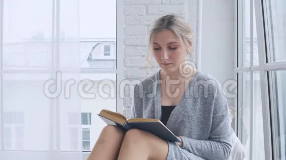 一个年轻的女孩坐在窗台上看书视频的预览图