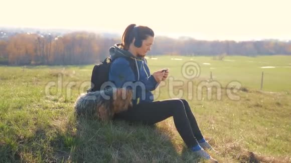 中年妇女和狗约克郡的游客带着背包在耳机里听音乐看着视频的预览图