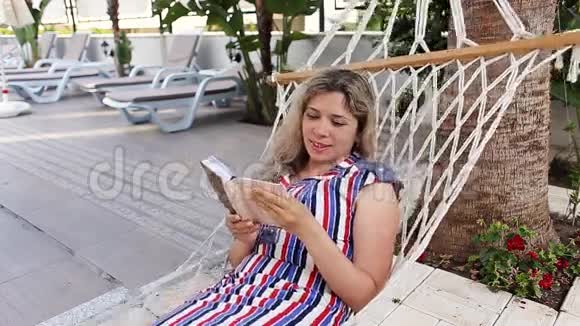 在游泳池附近的吊床上看书的女士视频的预览图
