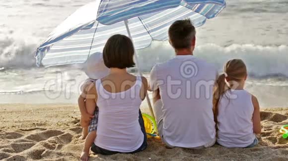 男人和女人带着两个孩子坐在沙滩上视频的预览图
