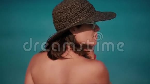 美丽的女人带着沙滩帽在海洋前微笑视频的预览图