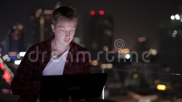 年轻的帅哥晚上用笔记本电脑观看城市景色视频的预览图