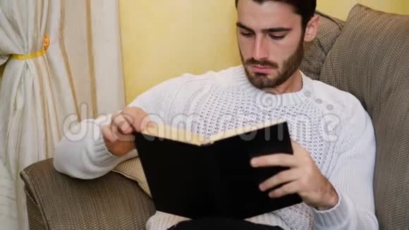 英俊的年轻人在家看书坐在沙发上视频的预览图