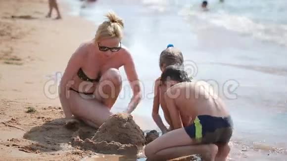 妈妈带着孩子在海滩上建造一座沙堡男孩和女孩视频的预览图