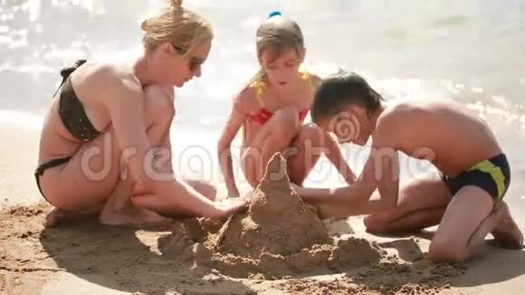 妈妈带着孩子在海滩上建造一座沙堡男孩和女孩视频的预览图