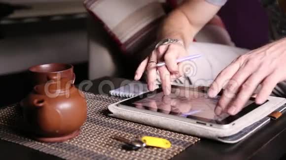 年轻的商人使用平板电脑进行网上购物并在笔记本上做笔记有人在电脑平板电脑和视频的预览图