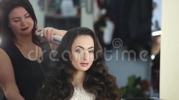 女性发型师正在为一位留着长发的漂亮黑发女郎制作芝加哥的波浪视频的预览图