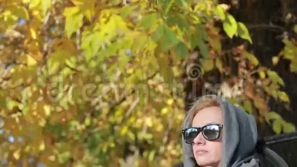 秋天公园里坐在长凳上戴太阳镜的漂亮女人黄叶视频的预览图