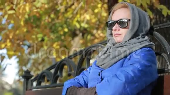 秋天公园里坐在长凳上戴太阳镜的漂亮女人黄叶视频的预览图