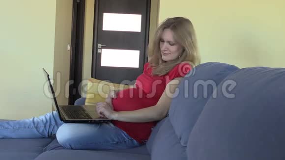 漂亮的孕妇爱抚肚皮和工作笔记本电脑视频的预览图