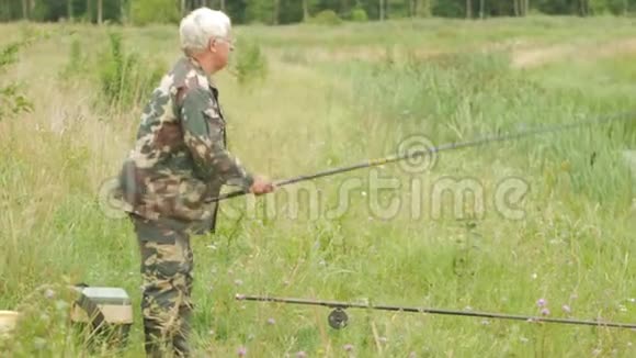 夏天一位老人正在一条小河上钓鱼使用鱼竿和蠕虫森林和高绿草视频的预览图