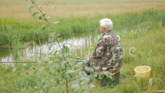 夏天一位老人正在一条小河上钓鱼使用鱼竿和蠕虫森林和高绿草视频的预览图