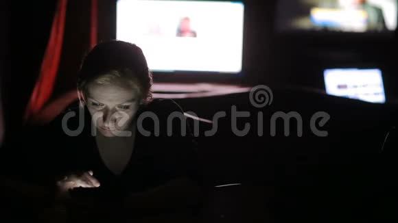 在电视屏幕背景下黑暗中看平板电脑的女人视频的预览图