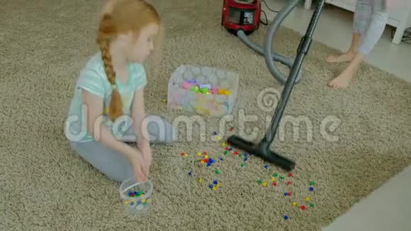 妈妈和女儿一个年轻的女人用吸尘器打扫卫生一个金发的小女孩收集玩具视频的预览图