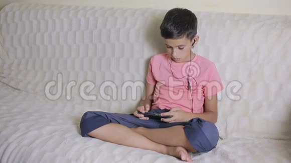 有智能手机和耳机的男孩在家听音乐或玩游戏视频的预览图