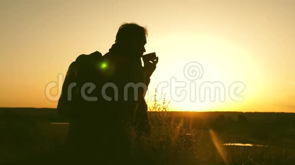 旅行者喝热茶看日落达到目标后休息坐在山顶上喝酒的孤独游客视频的预览图