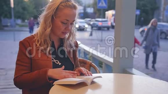 年轻的金发女人坐在街头咖啡馆的桌子旁看书视频的预览图