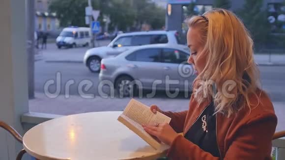 年轻的金发女人坐在街头咖啡馆的桌子旁看书视频的预览图