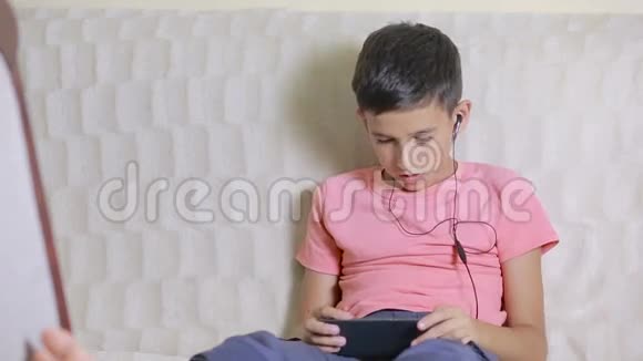 有智能手机和耳机的男孩在家听音乐或玩游戏视频的预览图