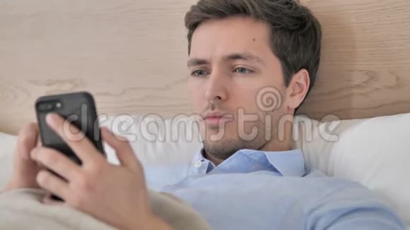 年轻人在床上使用智能手机视频的预览图