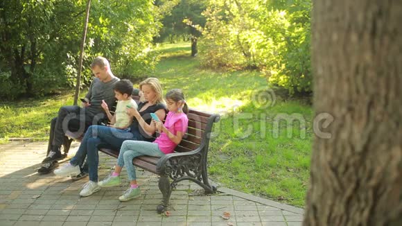 父母带着孩子坐在长凳上使用移动智能手机视频的预览图