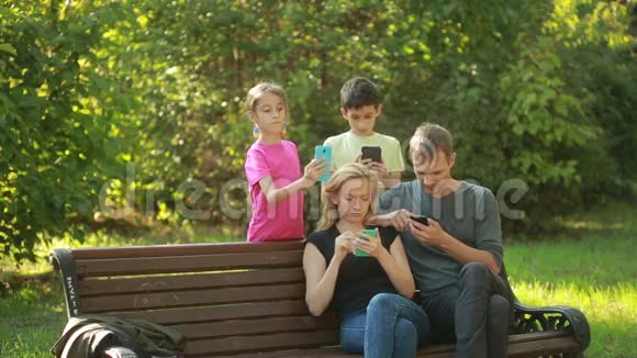 父母带着孩子坐在长凳上使用移动智能手机视频的预览图