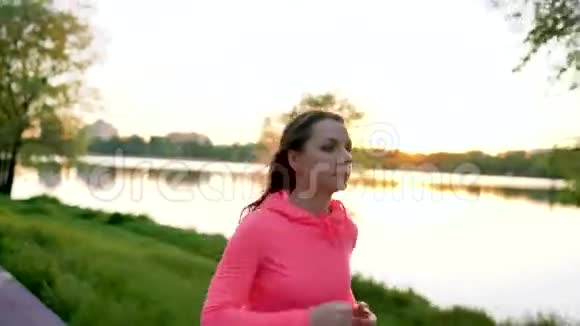 日落时分女人穿过湖岸的公园视频的预览图