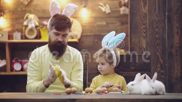 父子俩正在画蛋幸福的家庭正在为复活节做准备可爱的小男孩戴着兔子耳朵快乐视频的预览图