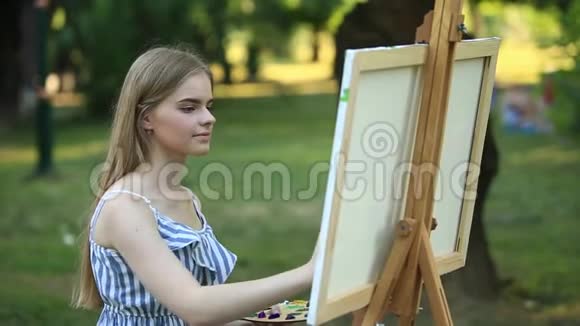 美丽的女孩坐在公园里用调色板和铲子画一幅画视频的预览图
