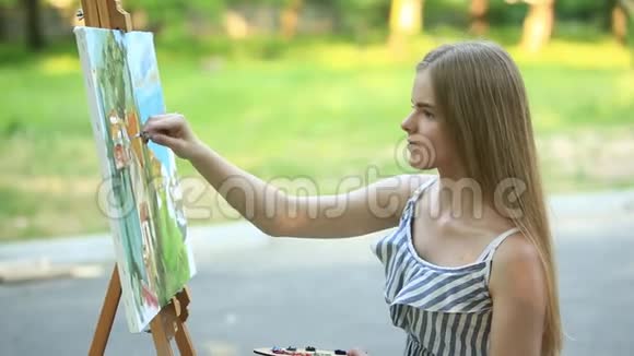 美丽的女孩坐在公园里用调色板和铲子画一幅画视频的预览图