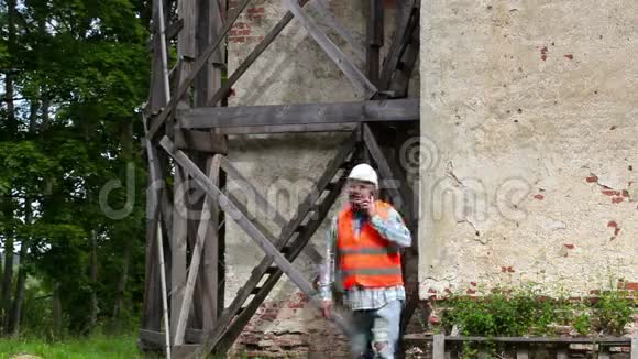 建筑工人在木脚手架附近用智能手机走路和说话视频的预览图